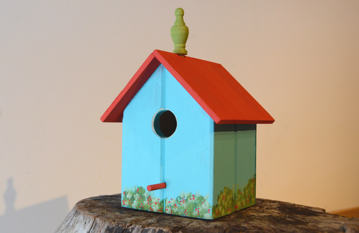 wooden birdhouse with a red roof, blue walls, and a green finial on top